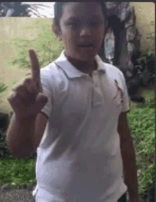 a young boy in a white polo shirt is giving a thumbs up .