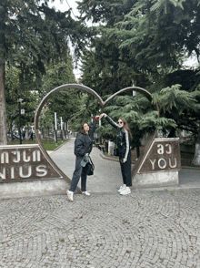 two women are posing in front of a heart shaped sculpture that says you