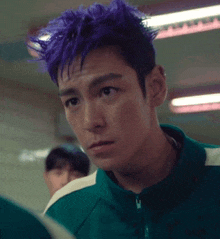 a man with purple hair is wearing a green jacket and looking at the camera .