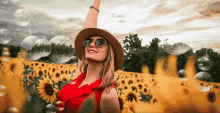 a woman wearing a hat and sunglasses stands in a field of sunflowers