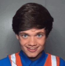 a young man wearing a blue shirt and an orange vest is smiling for the camera .