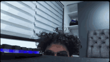 a man with curly hair is wearing sunglasses and peeking over a desk