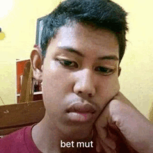 a young man is making a funny face with his hand on his face and the words bet mut written on his face .