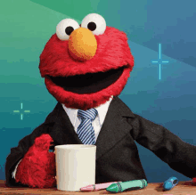 elmo is wearing a suit and tie while holding a cup of coffee