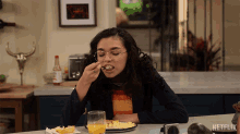 a woman sitting at a table with a plate of food and a glass of orange juice with netflix written on the bottom