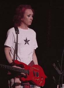 a man with red hair is playing a red guitar and wearing a white shirt with a star on it