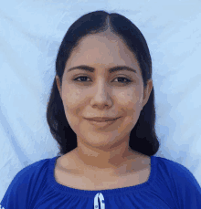 a woman wearing a blue shirt with a white button on the front smiles for the camera