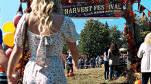 a woman in a white dress is walking in front of a sign that says welcome to the harvest festival .