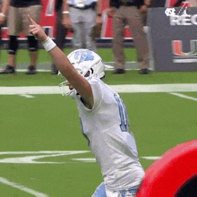 a football player wearing a white jersey and a blue helmet is giving a thumbs up on the field .