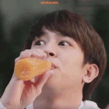 a young man is drinking a bottle of orange juice from a glass .