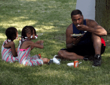 a man and two little girls are eating in the grass with a coke can in the foreground