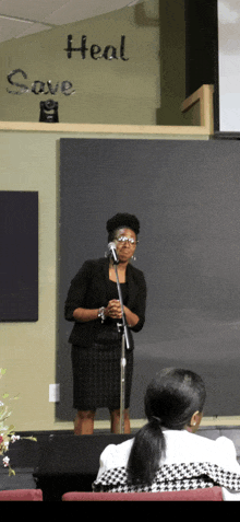 a woman stands in front of a microphone with the words heal save behind her