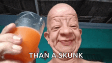 a bald man is holding a glass of orange juice with the words than a skunk below him