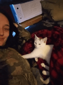 a white cat laying on a red blanket next to a person