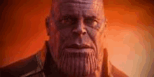 a close up of thanos ' face with a beard in front of a fire .