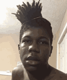 a shirtless young man with dreadlocks in a bun is looking at the camera .