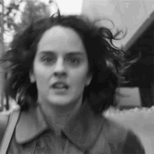 a woman with her hair blowing in the wind is walking down a street in a black and white photo .