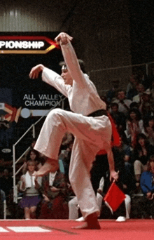 a man in a white karate uniform is doing a kick in front of a sign that says all valley champion