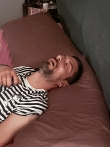 a man in a striped shirt is laying on a bed with his eyes closed