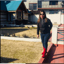 a woman in a black jacket and red boots is standing in front of a house