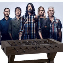 a group of men standing next to each other with a foosball table in the middle