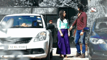 a man and woman are standing in front of a white car with a license plate that says 12 kl 6540