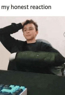 a young man is sitting at a desk with his hand on his head and a keyboard in front of him .