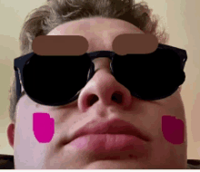 a man wearing sunglasses has pink spots painted on his cheeks