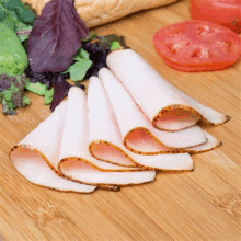 sliced turkey breast is sitting on a wooden cutting board next to vegetables .