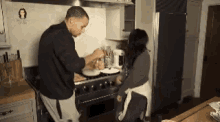 a man and a woman are cooking in a kitchen with a picture of a woman on the wall behind them