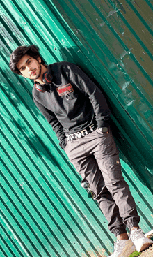 a young man leaning against a green wall wearing headphones and a sweatshirt that says ' nothing ' on it