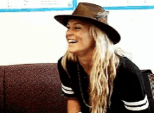 a woman wearing a hat and a black shirt is sitting on a couch and smiling .