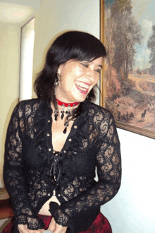 a woman wearing a black lace top laughs in front of a framed painting