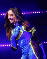 a woman in a blue and yellow outfit is smiling and holding her hand to her chest