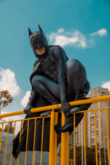 a man in a batman costume is climbing a yellow railing