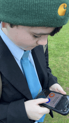 a boy wearing a green carhartt hat is looking at a phone