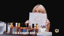 a woman is holding up a drawing of a man and woman behind a table full of hot sauce bottles