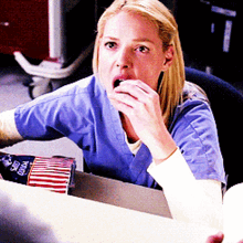 a woman in a blue scrub top is sitting at a desk with an american flag in front of her