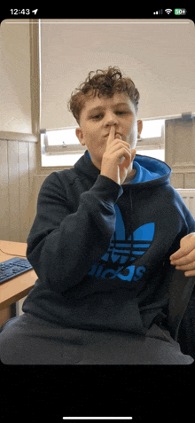 a young man wearing an adidas hoodie holds his finger to his nose