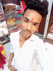 a man with a red bindi on his forehead stands in front of a stack of clothes