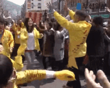 a group of people in yellow jackets are dancing on a street with a sign that says ' a ' on it