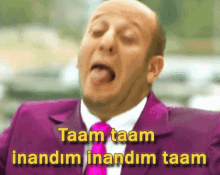 a bald man in a purple suit and pink tie says taam taam