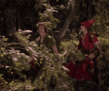 a man in a red hat is standing next to a woman in a green dress in a forest .