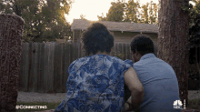 a man and a woman are sitting in front of a wooden fence with a nbc logo on the bottom