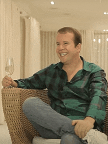 a man in a plaid shirt is sitting on a wicker chair holding a glass of wine