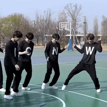 a group of young men are dancing on a basketball court wearing black shirts with the letter n and w on them