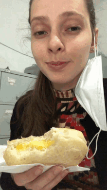 a woman wearing a face mask is holding a sandwich