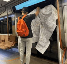 a man with an orange backpack is looking at a map on the train