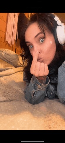 a woman wearing headphones and a denim jacket is laying on a bed and making a face