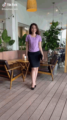 a woman in a purple shirt and black skirt is standing in front of a table and chairs in a restaurant ..